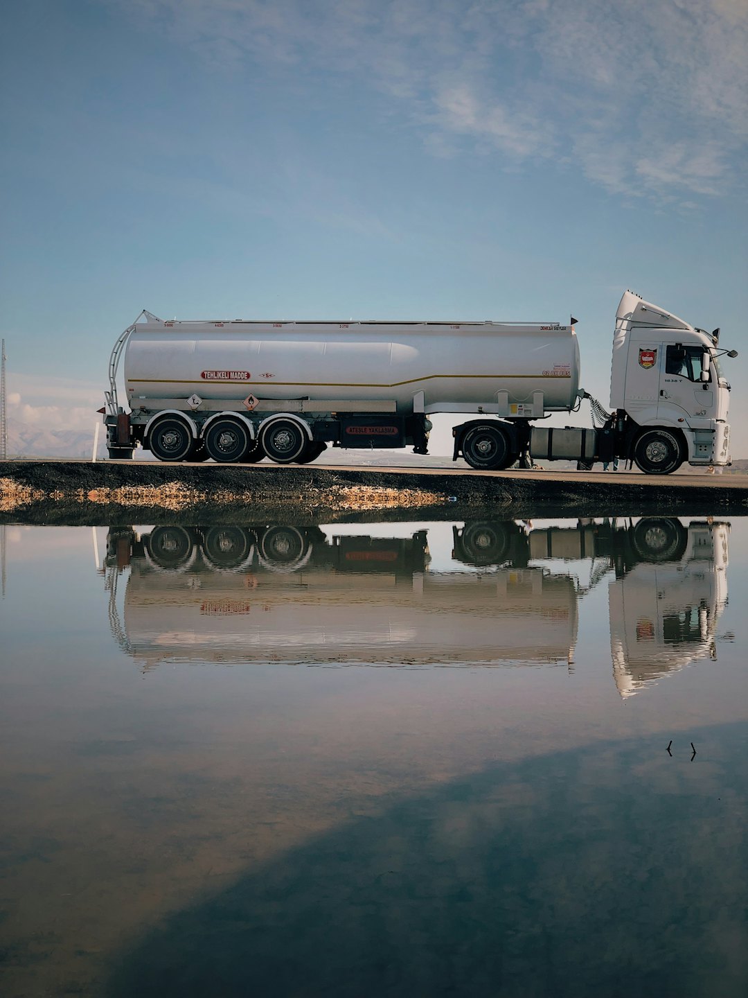 A white tanker truck parked beside a still lake.