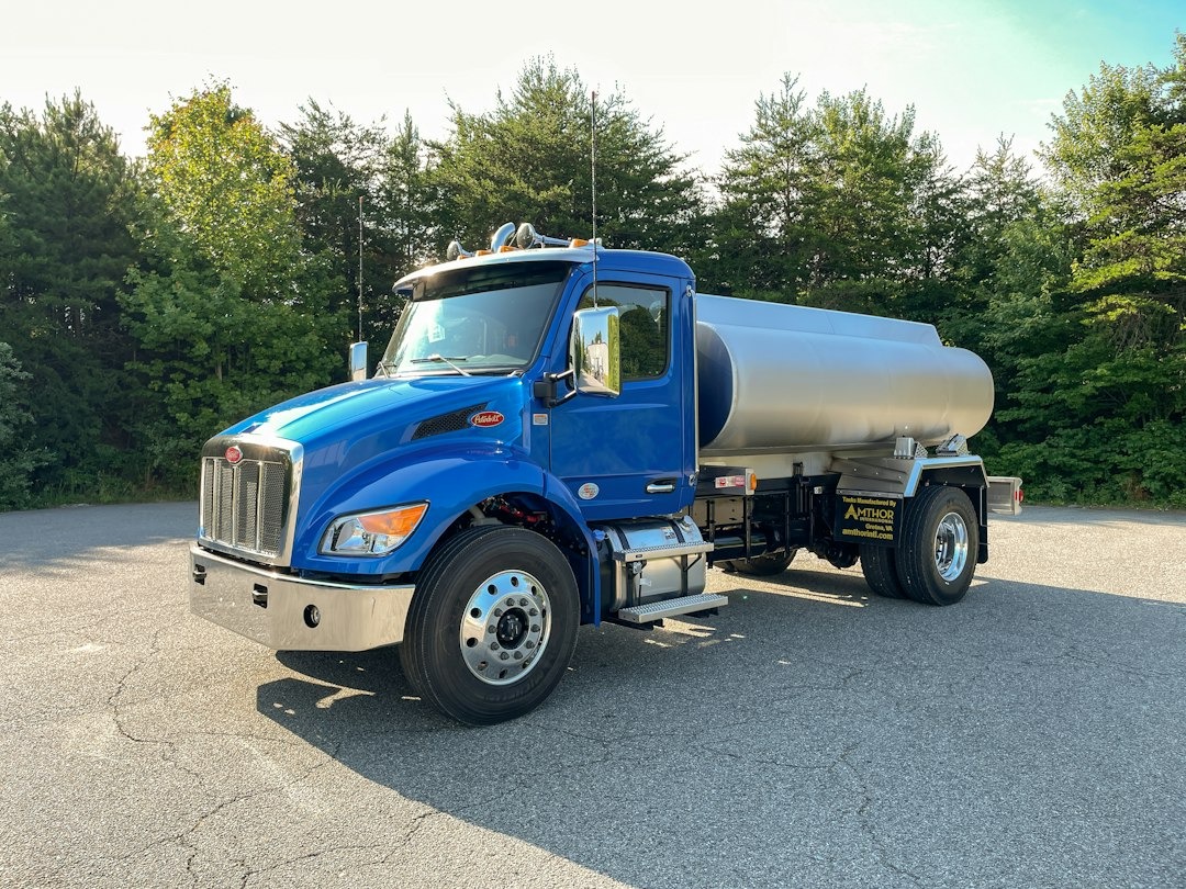 Blue tanker truck parked on an asphalt lot near trees.